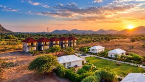 Un complejo turístico con varias edificaciones, un jardín ajardinado y vistas a montañas distantes.