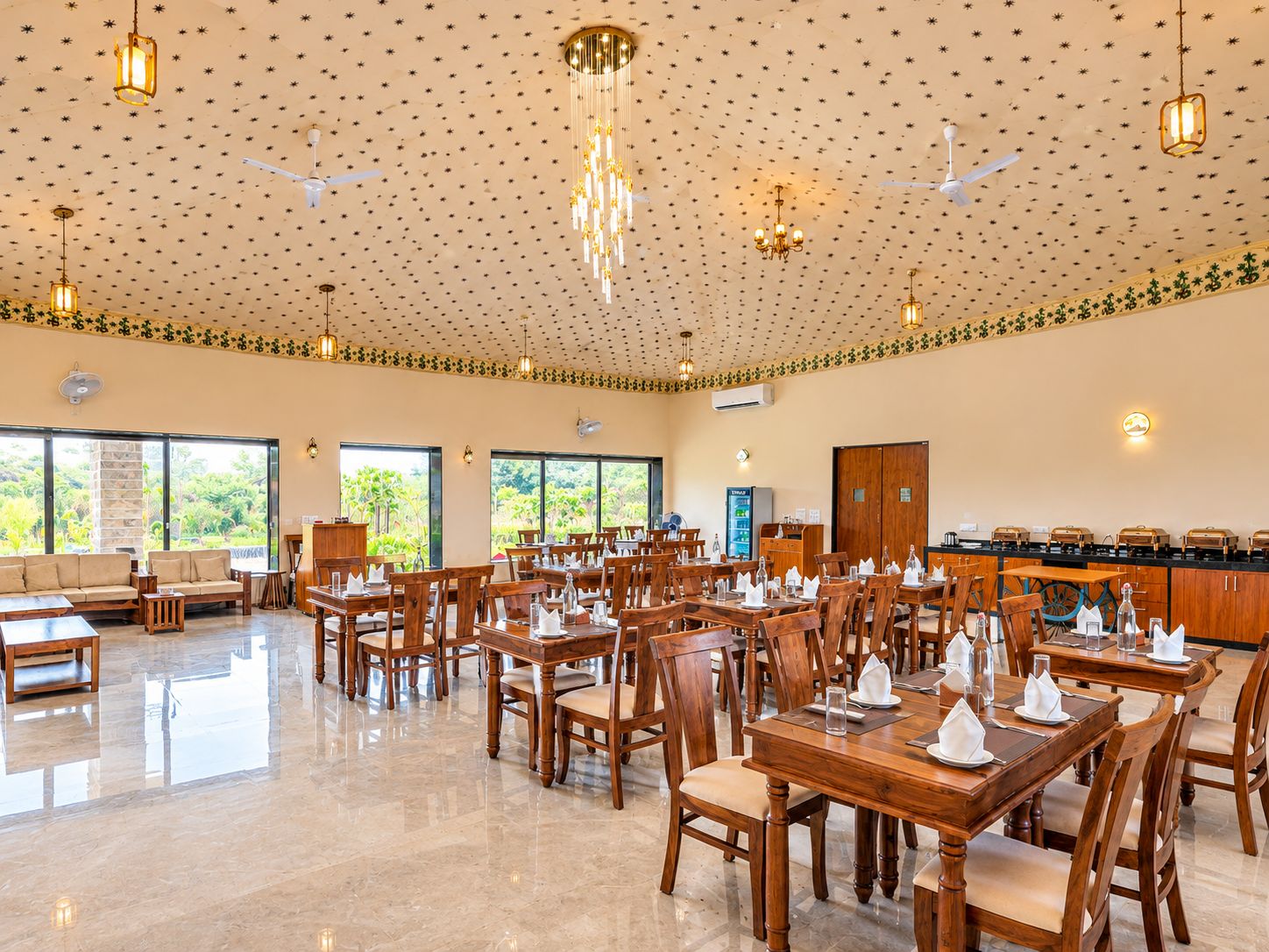 Un vaste espace dédié à la salle à manger, avec des tables et des chaises en bois, des ventilateurs de plafond et un plafond décoratif orné de motifs en forme d’étoiles.