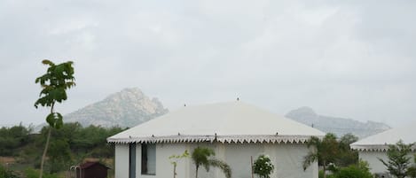 A white tent with a peaked roof, surrounded by greenery and a mountainous backdrop.