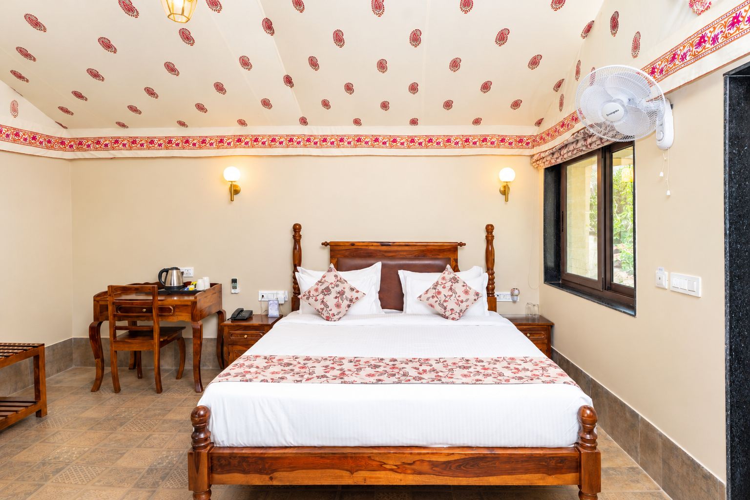 A hotel room with a wooden bed, a desk with a chair, a bedside table, and a window.