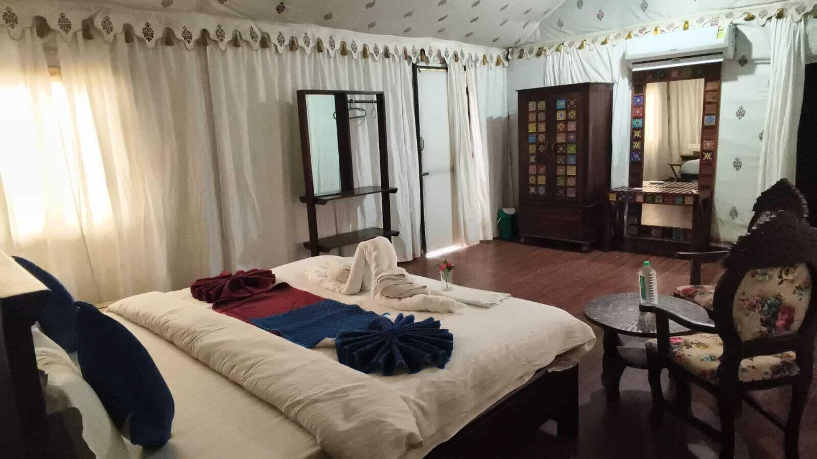 A hotel room with a bed, a small table, a chair, a wardrobe, and a mirror.