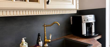A kitchen with a modern coffee machine, a sink with a gold faucet, and a bottle of hand soap.