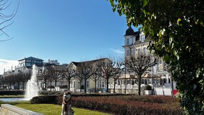 Um parque com uma fonte, uma estátua e edifícios ao fundo.