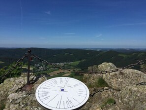 Señal informativa circular con flechas direccionales, una cerca de malla y una vista panorámica de un valle.