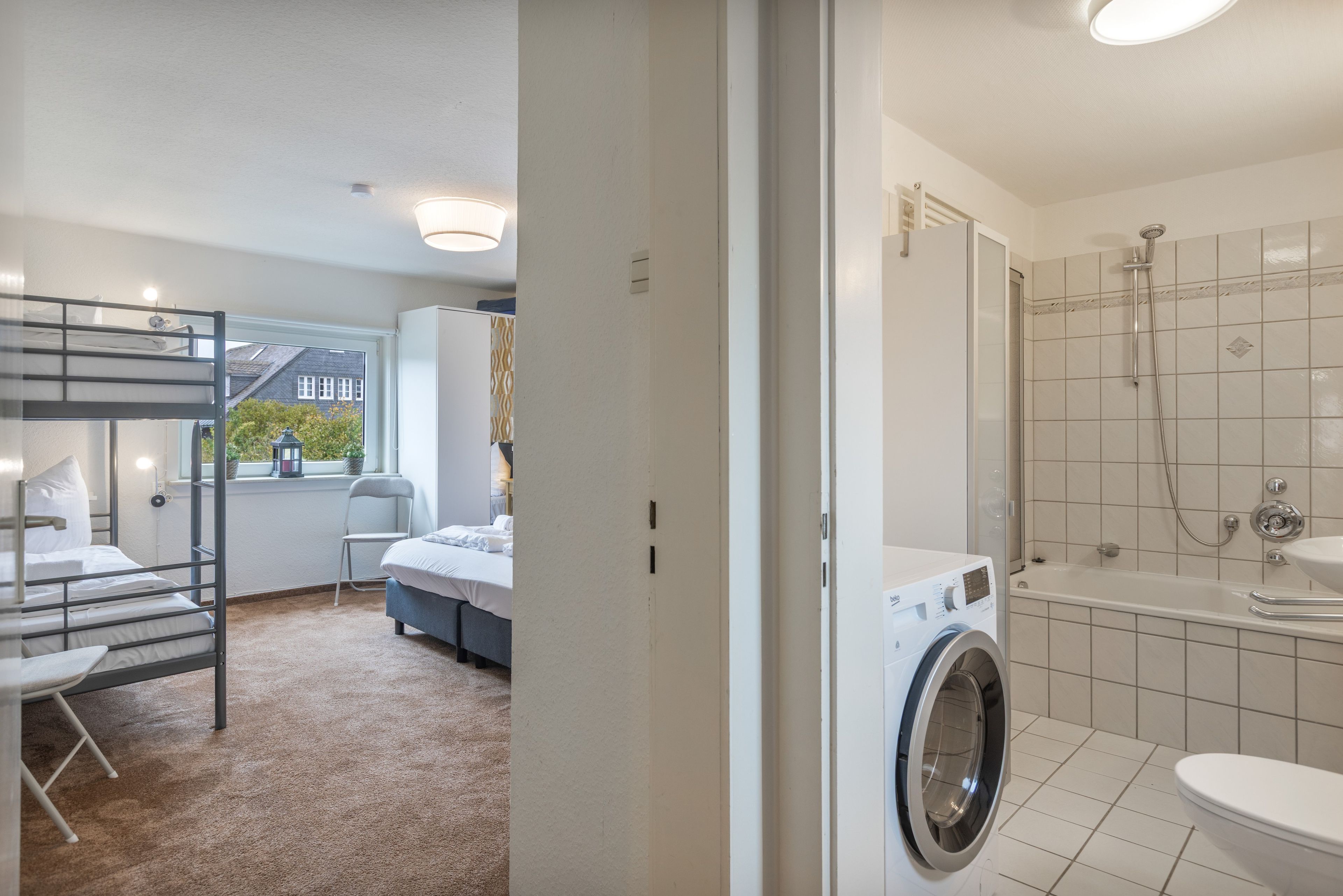 A hotel room with a bunk bed, a single bed, a washing machine, a shower, and a bathroom with a toilet and sink.