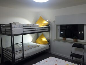 Ein Schlafraum mit Etagenbetten, einem Fenster, einem Stuhl und einem kleinen Tisch.