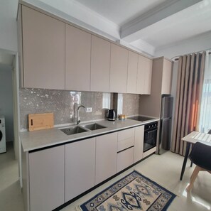 A modern kitchen with a central island, built-in appliances, and a dining area with a chair. - Kypsel Apartment – Your Cozy Beach Getaway in Durrës (Durrës)