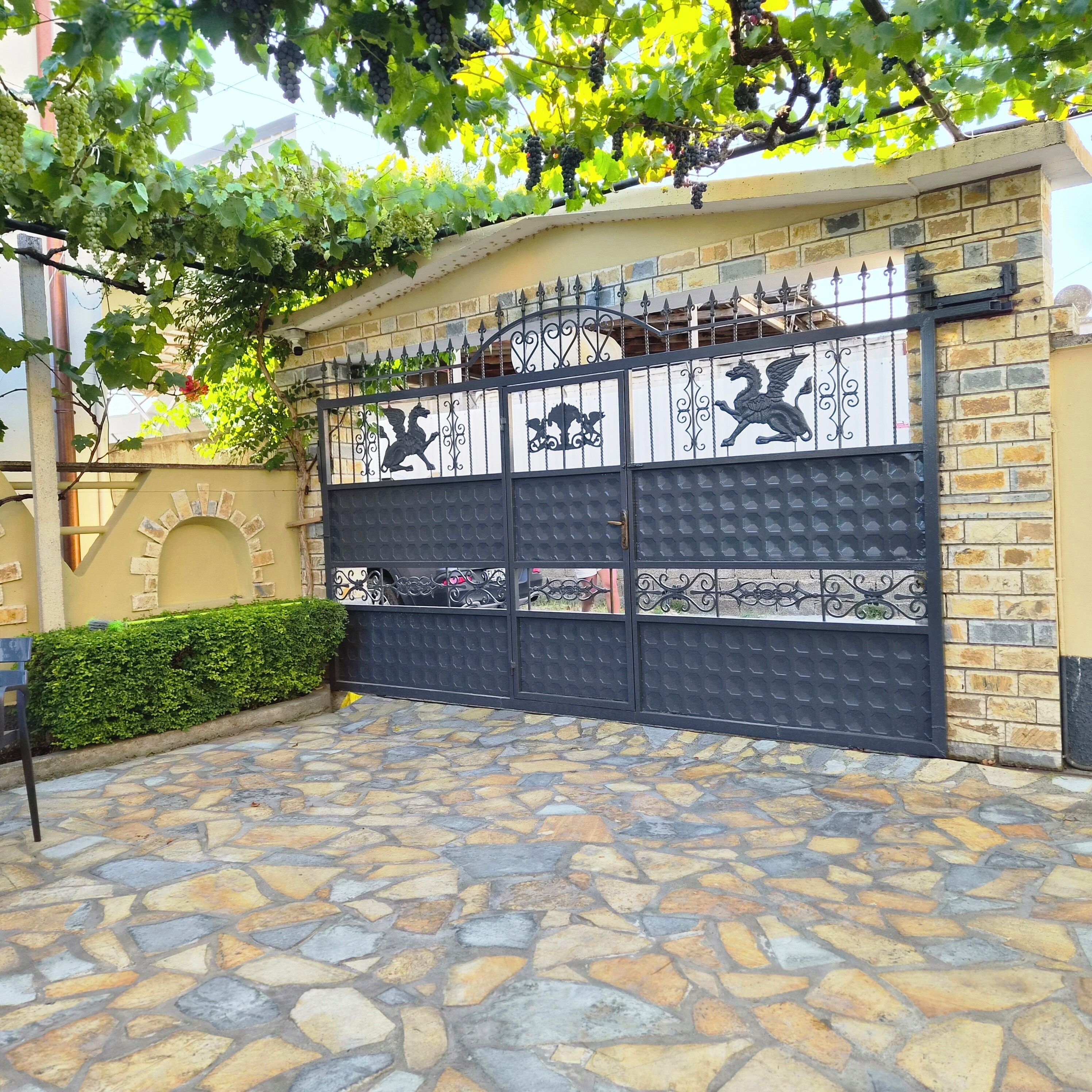 A gated entrance with decorative metalwork, a stone-paved driveway, and a brick wall.