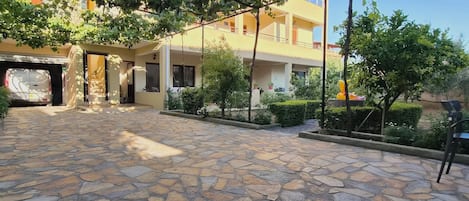 A courtyard with stone flooring, a building with balconies, and greenery.