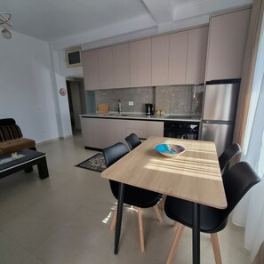 Eine moderne Küche mit Essbereich, ausgestattet mit einem Holztisch und schwarzen Stühlen, einem Kühlschrank und einer Spüle.