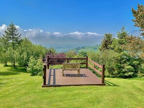 Una terraza de madera con un banco, rodeada de exuberante vegetación y una vista panorámica.