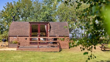 A wooden cabin with a brick roof, a glass door, and a small deck with seating.