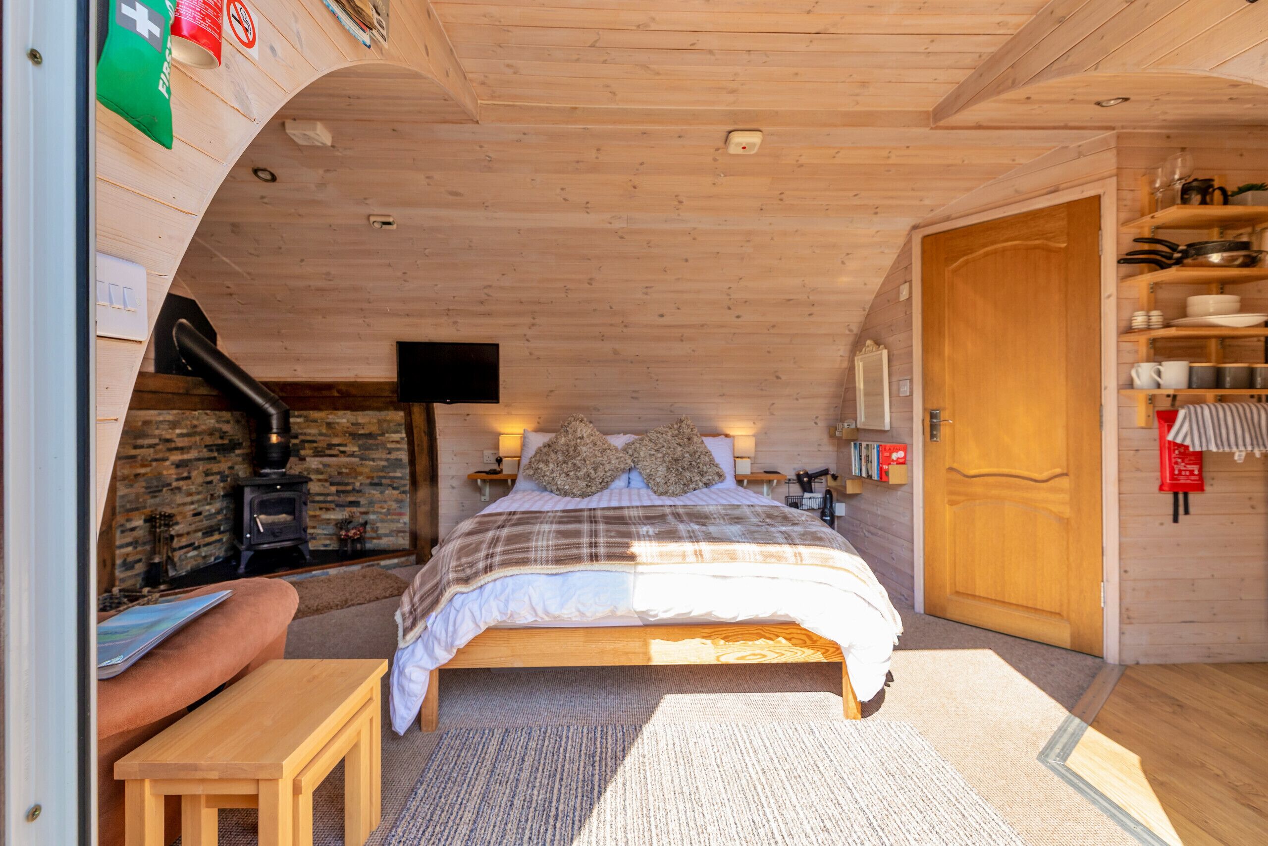 A cozy wooden room with a bed, a fireplace, and a wooden door.