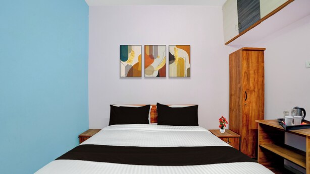 A hotel room with a bed, a wooden wardrobe, a nightstand, and three abstract paintings on the wall. - Collection O Westhill Near Govt Engg (Kozhikode)