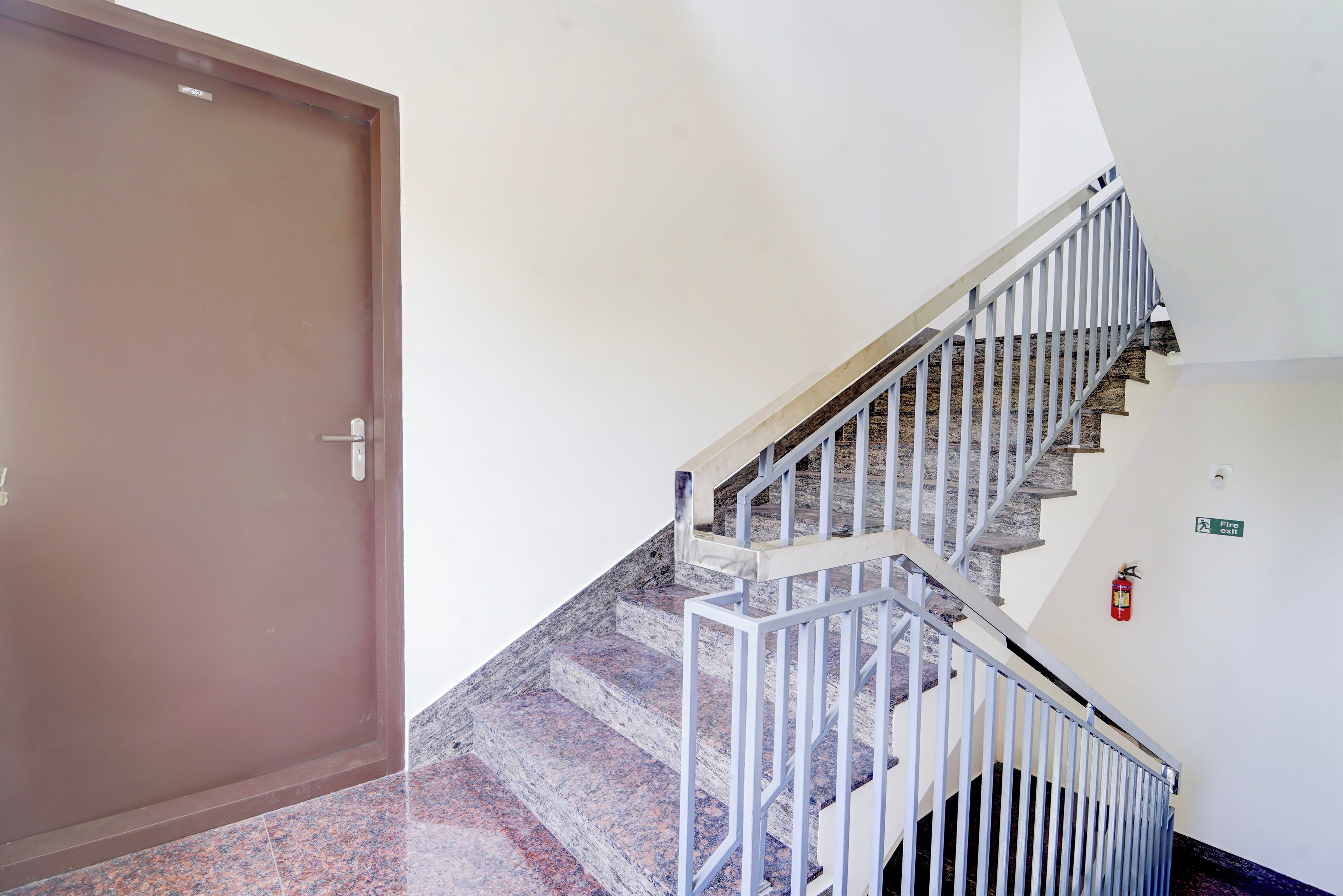 A staircase with metal railings leading to a landing, a fire exit sign, and a closed door.
