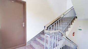 A staircase with metal railings leading to a landing, a fire exit sign, and a closed door.
