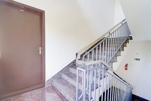 A staircase with metal railings leading to a landing, a fire exit sign, and a closed door. - Collection O Westhill Near Govt Engg (Kozhikode)