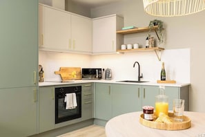 A modern kitchen with a built-in oven, a microwave, a sink, and a wooden cutting board. - Pelican House One | Luxury Apartment | 6 Min Walk to Beach | Bournemouth Centre (Bournemouth)