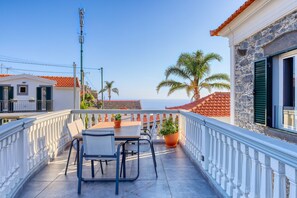 Ein Balkon mit Tisch und Stühlen, einem Blumentopf und Blick aufs Meer.