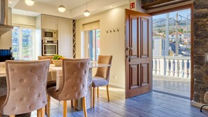 A modern kitchen with built-in appliances, a dining area with upholstered chairs, and a balcony with a stone wall. - Casa São Tiago, a Home in Madeira (Ponta do Sol)