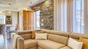 A modern living room with a beige sectional sofa, a stone accent wall, and a view of the outside. - Casa São Tiago, a Home in Madeira (Ponta do Sol)