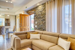 Ein modernes Wohnzimmer mit einem beigefarbenen Ecksofa, einer Wand aus Naturstein und Blick ins Freie.