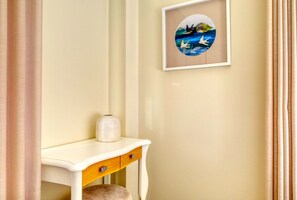 Una stanza con una scrivania bianca, un quadro appeso al muro e una tenda parzialmente visibile.