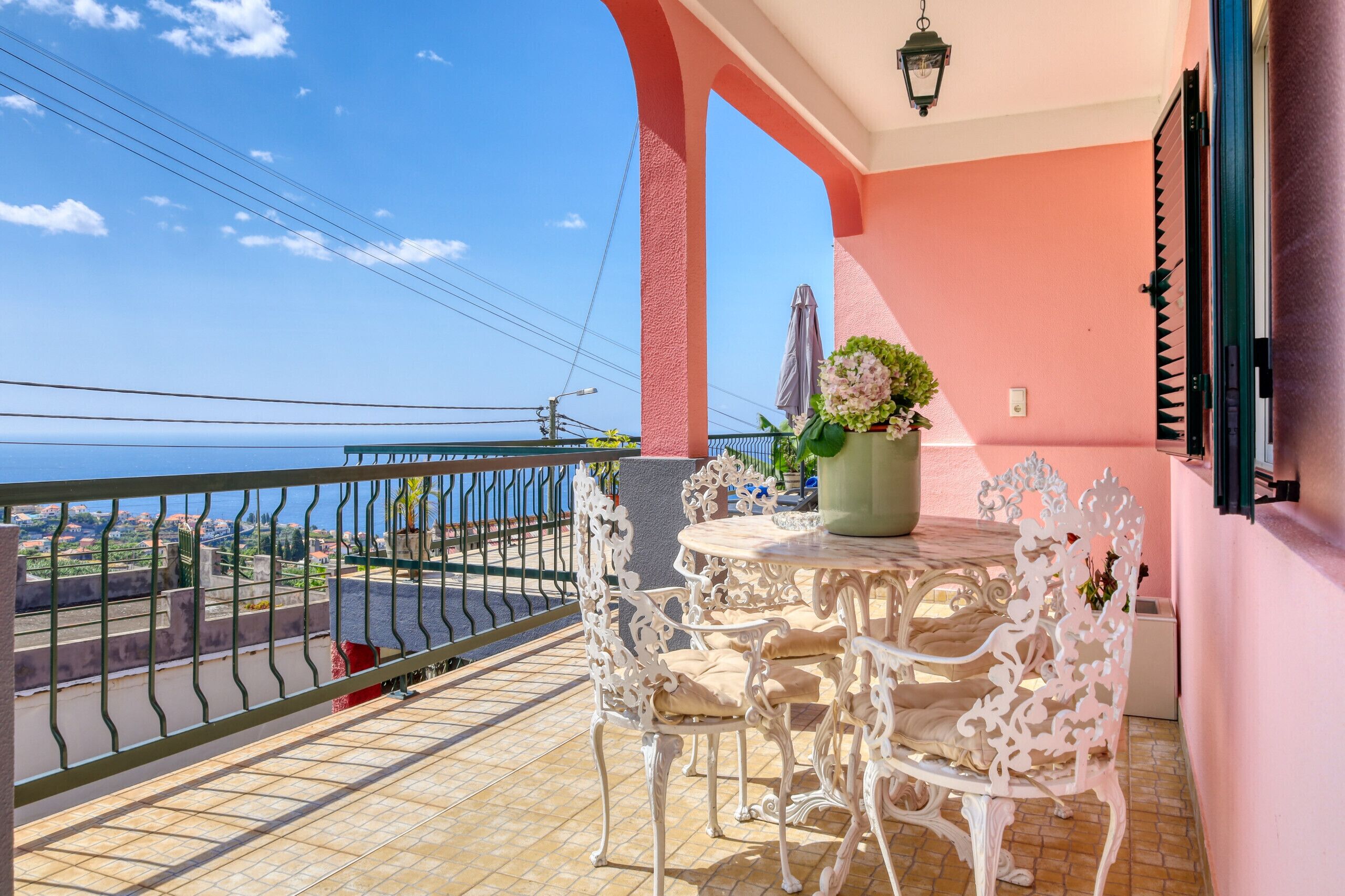 Ein Balkon mit Tisch und Stühlen, einer Topfpflanze und Blick auf das Meer.