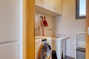 A laundry room with a front-loading washing machine, a drying rack, and a mop. - Casa do Serrado, a Home in Madeira (Ponta do Sol)