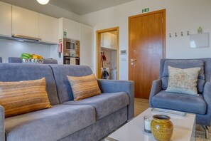 A modern living room with a sofa, armchair, and a coffee table. There is a kitchen area with a microwave and oven. - Casa do Serrado, a Home in Madeira (Ponta do Sol)
