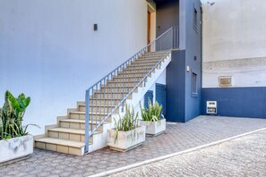 Eine Treppe führt zu einem Hauseingang, am Fuß befinden sich Kübelpflanzen.