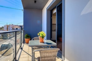 Ein Balkon mit Tisch, Stühlen, zwei Blumentöpfen und Blick auf die Straße.