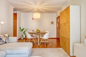 A modern living room with a sofa, a dining table with chairs, a hanging light fixture, and a wooden cabinet. - Cozy Santa Cruz, a Home in Madeira (Santa Cruz)