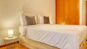 A bedroom with a bed, bedside table, lamp, and a wooden wardrobe. - Cozy Santa Cruz, a Home in Madeira (Santa Cruz)