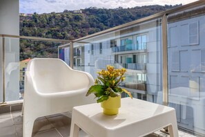 Ein Balkon mit einem weißen Plastikstuhl und einem kleinen Tisch mit einem gelben Blumentopf.