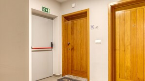A hallway with a wooden door, a red emergency exit sign, and a 'HOME' mat. - Cozy Santa Cruz, a Home in Madeira (Santa Cruz)
