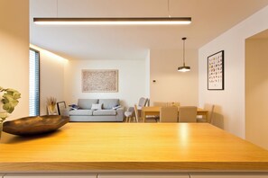 A modern living room with a wooden dining table, a grey sofa, and a dining area with chairs. - Modern & Comfortable Brand-New 3-Bedroom Apartment with AC and Parking, Near the Metro and Downtown (Porto)