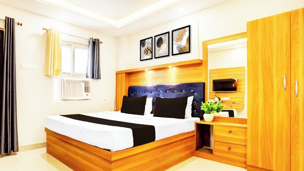 A modern bedroom with a wooden bed frame, a built-in wardrobe, a bedside table with a plant, and a large mirror. - Super Collection O Gola Road (Danapur)