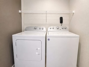 A laundry room with two white Whirlpool washers and dryers, a white wall, and a metal shelf above the dryers. - Eagles Nest at Lands End - Boat Slip! (Osage Beach)