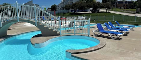 A swimming pool with a curved design, a gated entrance, and blue lounge chairs along the poolside.