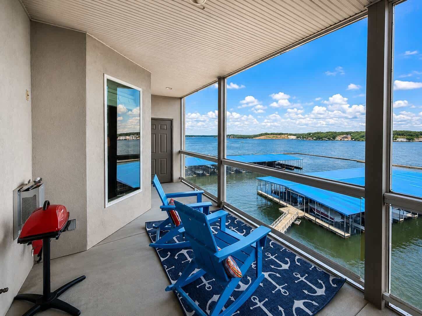 A balcony with a view of a marina, a red chair, and a blue chair with a nautical-themed rug.