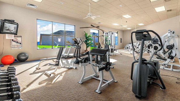 Une salle de sport équipée de matériel d’exercice, dotée de grandes fenêtres et d’un ventilateur au plafond.