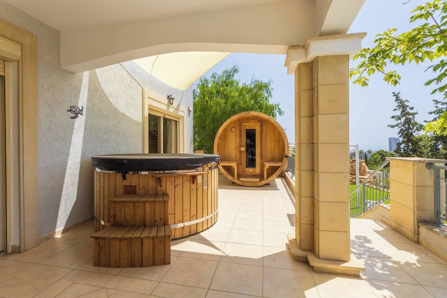 Un área de spa con un jacuzzi de madera y sauna, un patio cubierto y vistas al verdor.