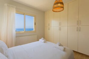 Une chambre avec une grande fenêtre, un lit recouvert de draps blancs et une armoire.