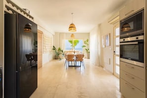 Une cuisine moderne avec un coin repas, comprenant un grand îlot central, des appareils électroménagers intégrés et une vue sur l’extérieur.