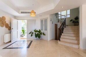 Un hall d’entrée spacieux, agrémenté d’une grande plante en pot, d’un escalier et d’un luminaire décoratif au plafond.