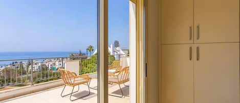 Un balcon avec des fauteuils en osier, une vue sur la mer et une armoire blanche.