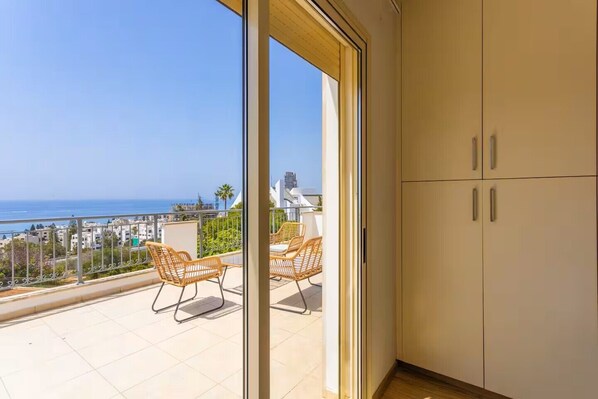 Un balcon avec des fauteuils en osier, une vue sur la mer et une armoire blanche.