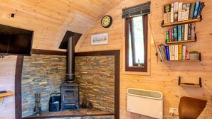 L’intérieur chaleureux d’un chalet avec une cheminée en pierre, une bibliothèque et une horloge au mur.