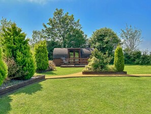 A well-maintained garden with a wooden deck, a small cabin, and a variety of trees.